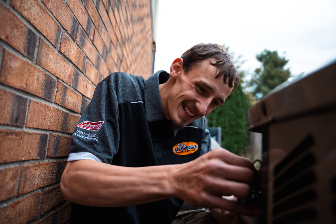 Rick's Affordable technician smiling while performing AC maintenance on an outdoor unit
